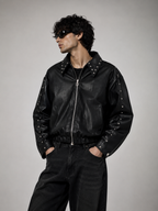 Male model sitting on a chair wearing the XOVRA Ironbite black studded cropped jacket in a luxury editorial fashion shoot.